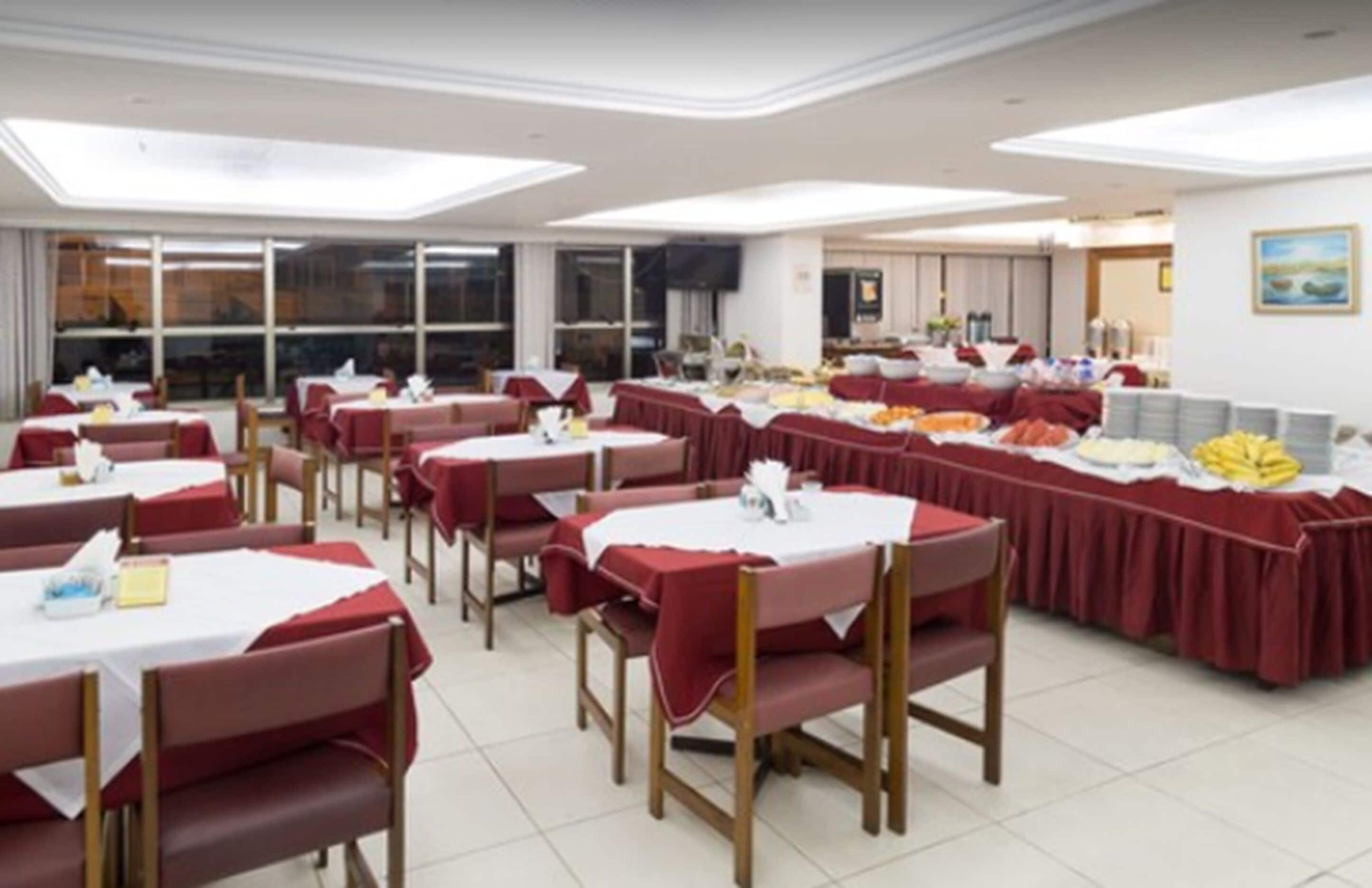 A dining area with multiple tables and chairs, a buffet setup, and a large window providing natural light.