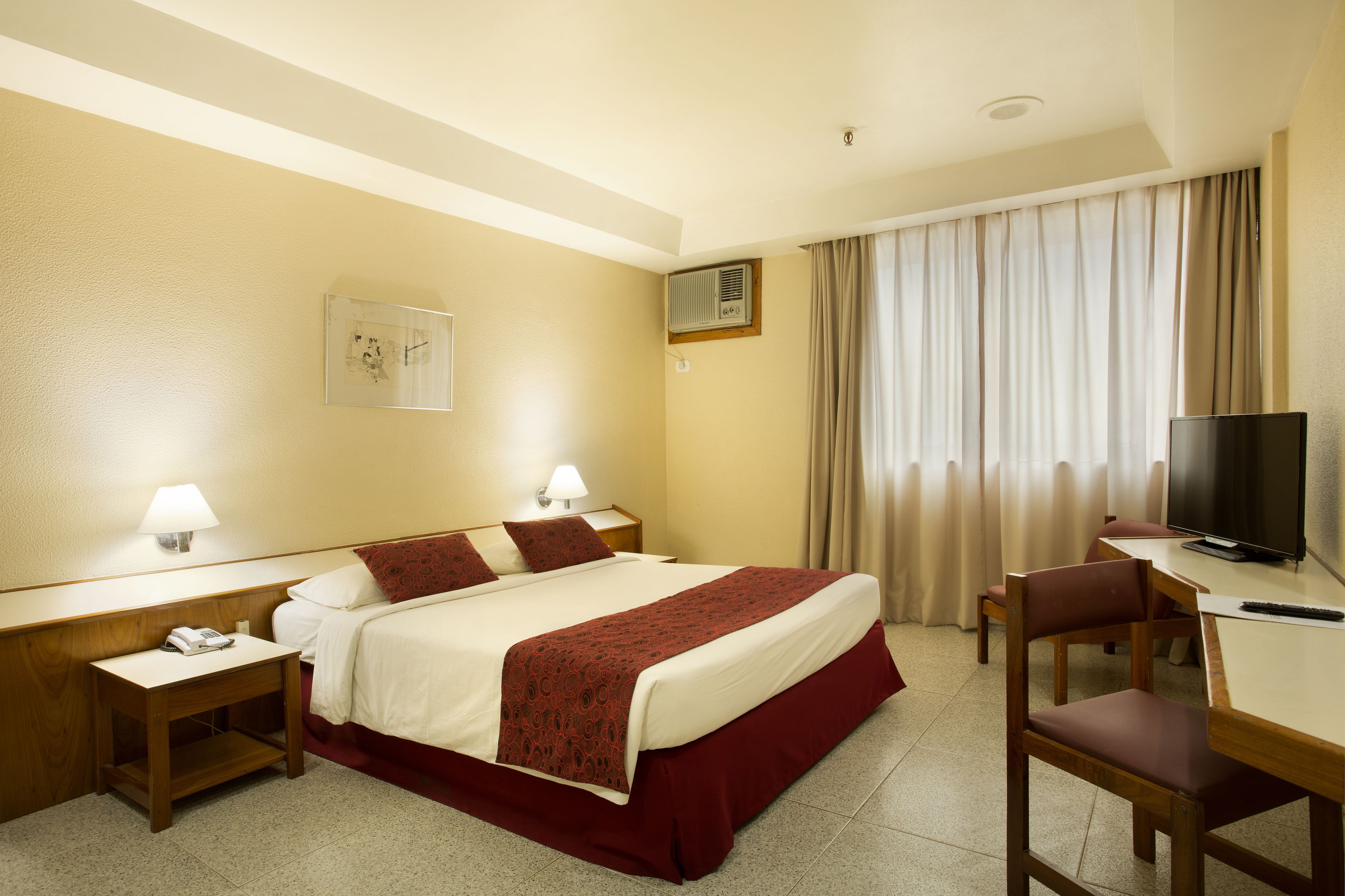 A hotel room with a bed, a desk with a chair, a television, and a lamp.