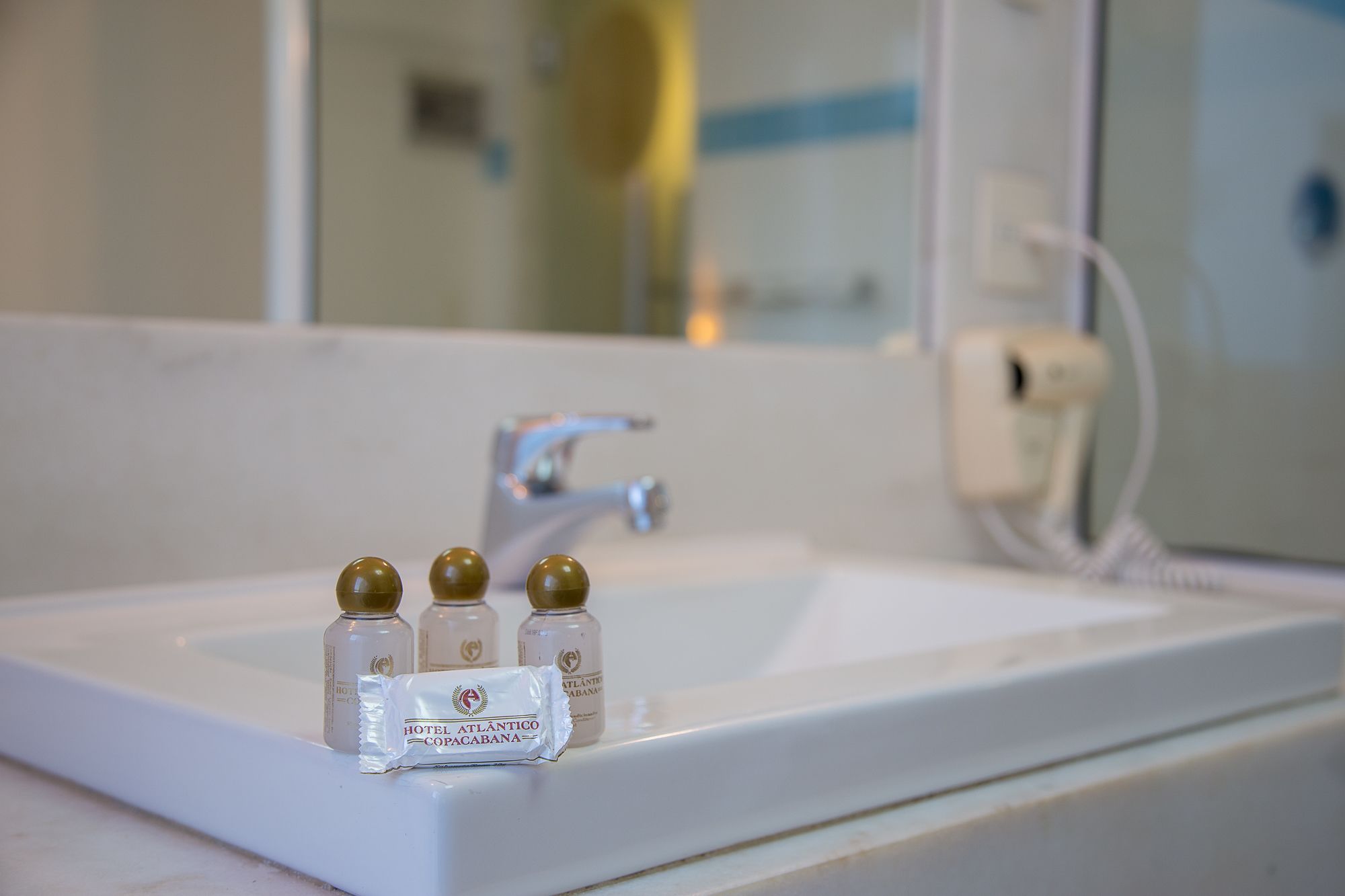 A bathroom sink with three bottles of Hotel Atlantico Copacabana soap.