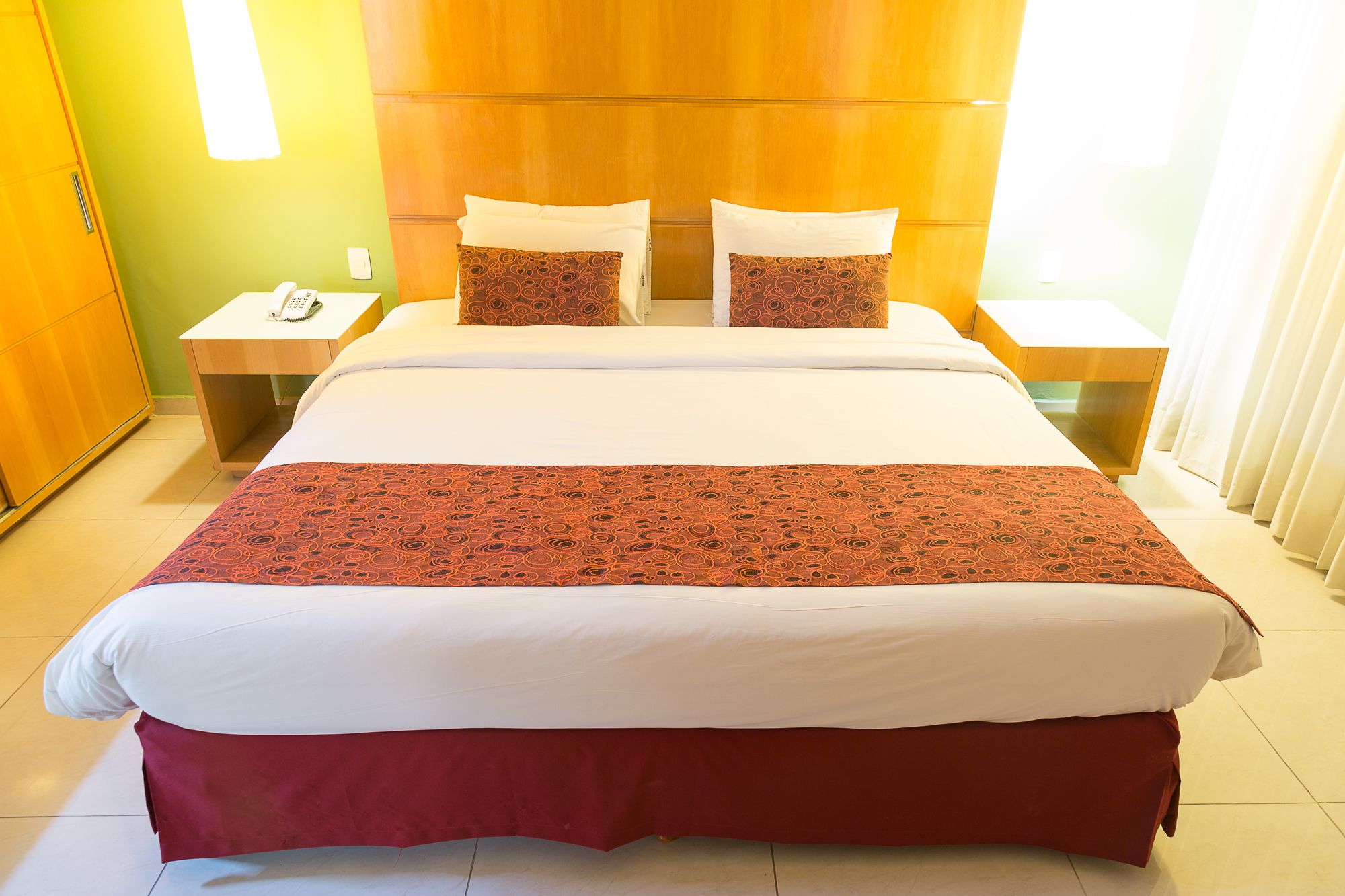 A hotel room with a large bed, two bedside tables, a telephone, and a green wall.