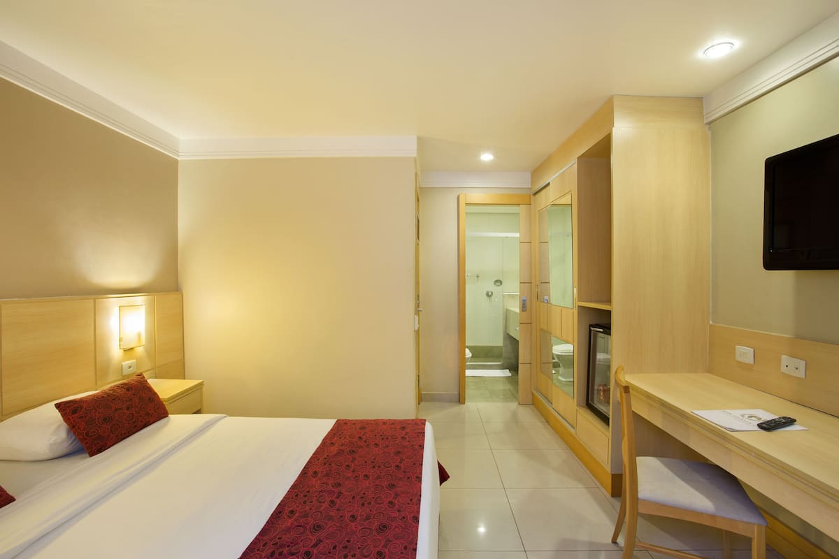 Ein Hotelzimmer mit Bett, Nachttisch, Lampe, Schreibtisch, Stuhl und Fernseher.