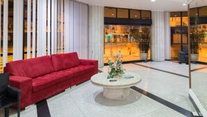 Un hall d’entrée moderne avec un canapé rouge, une table basse ronde et une cloison en verre donnant sur la rue.