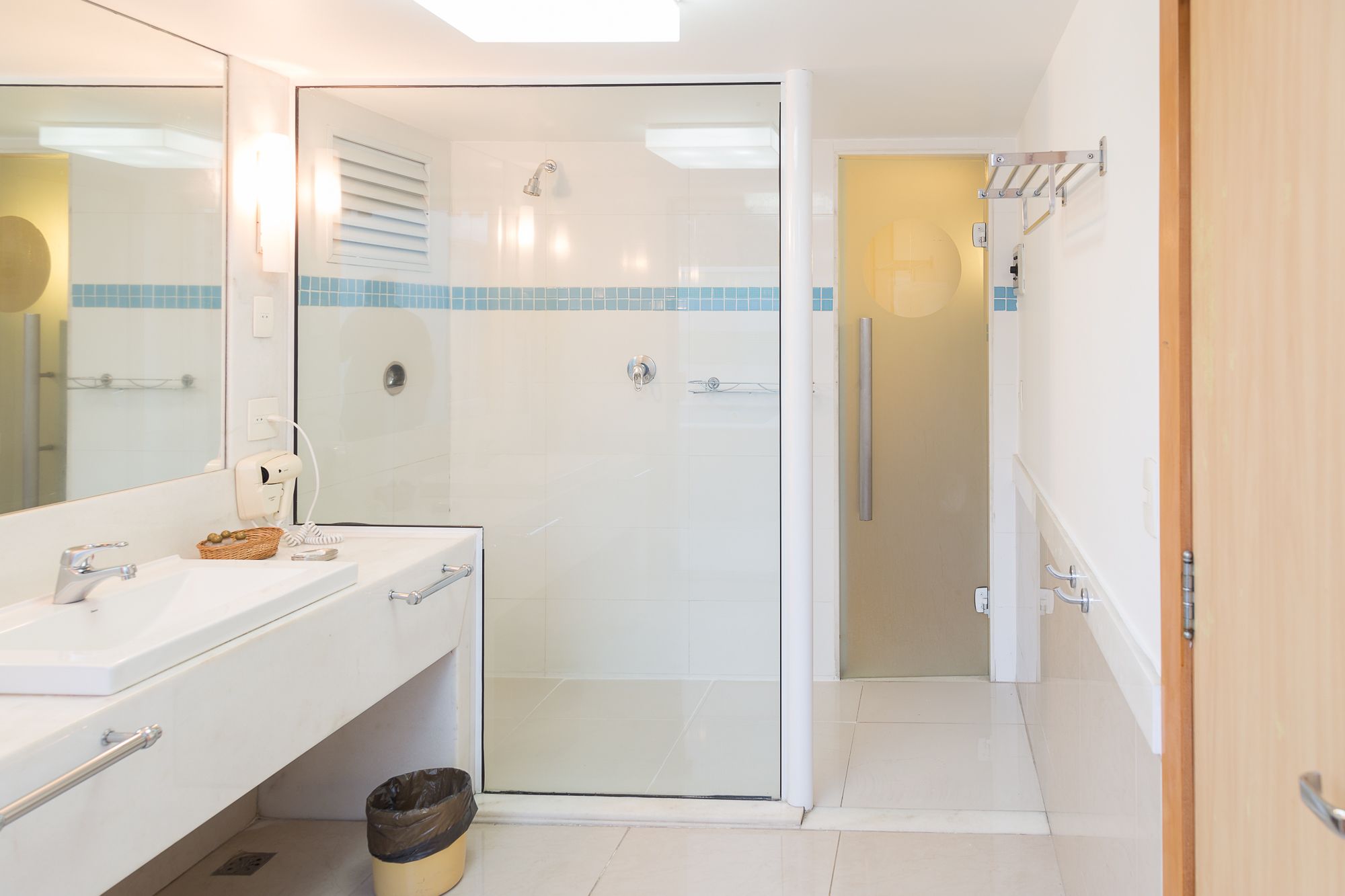 A modern bathroom with a glass shower enclosure, a white sink with a basket of toiletries, and a towel rack.