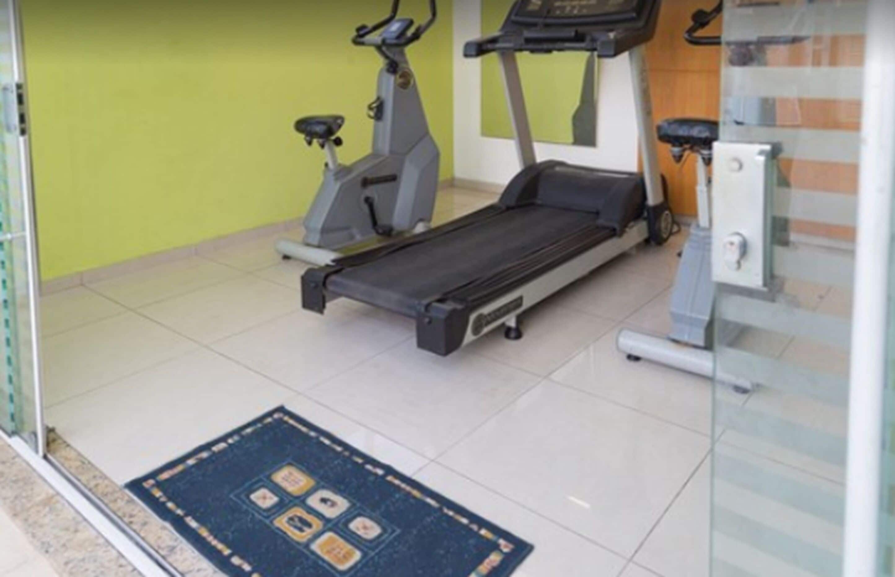 Een sportschool met een loopband, elliptische trainer en hometrainer.