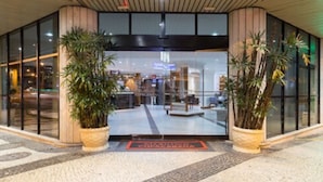 Une entrée d’hôtel moderne avec des portes en verre, des plantes en pot et un sol carrelé.