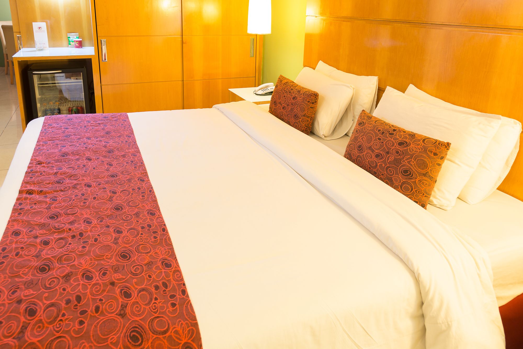 Une chambre d’hôtel avec un grand lit, une table de chevet, un réfrigérateur et une lampe fixée au mur.