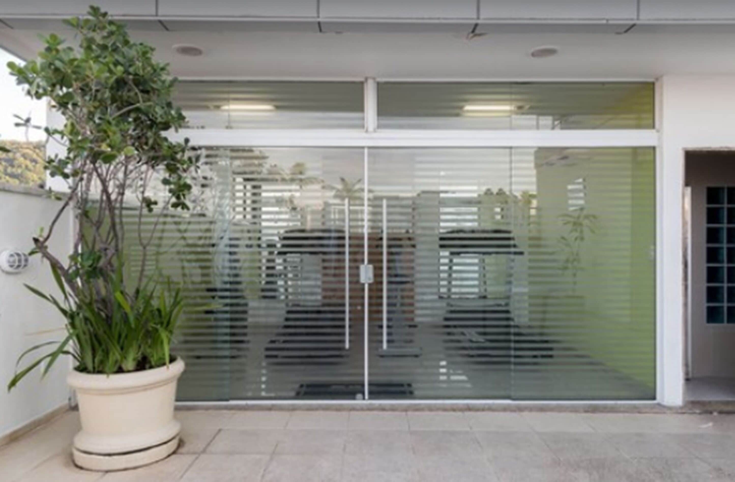A modern building entrance with a glass door, a potted plant, and a metal gate.