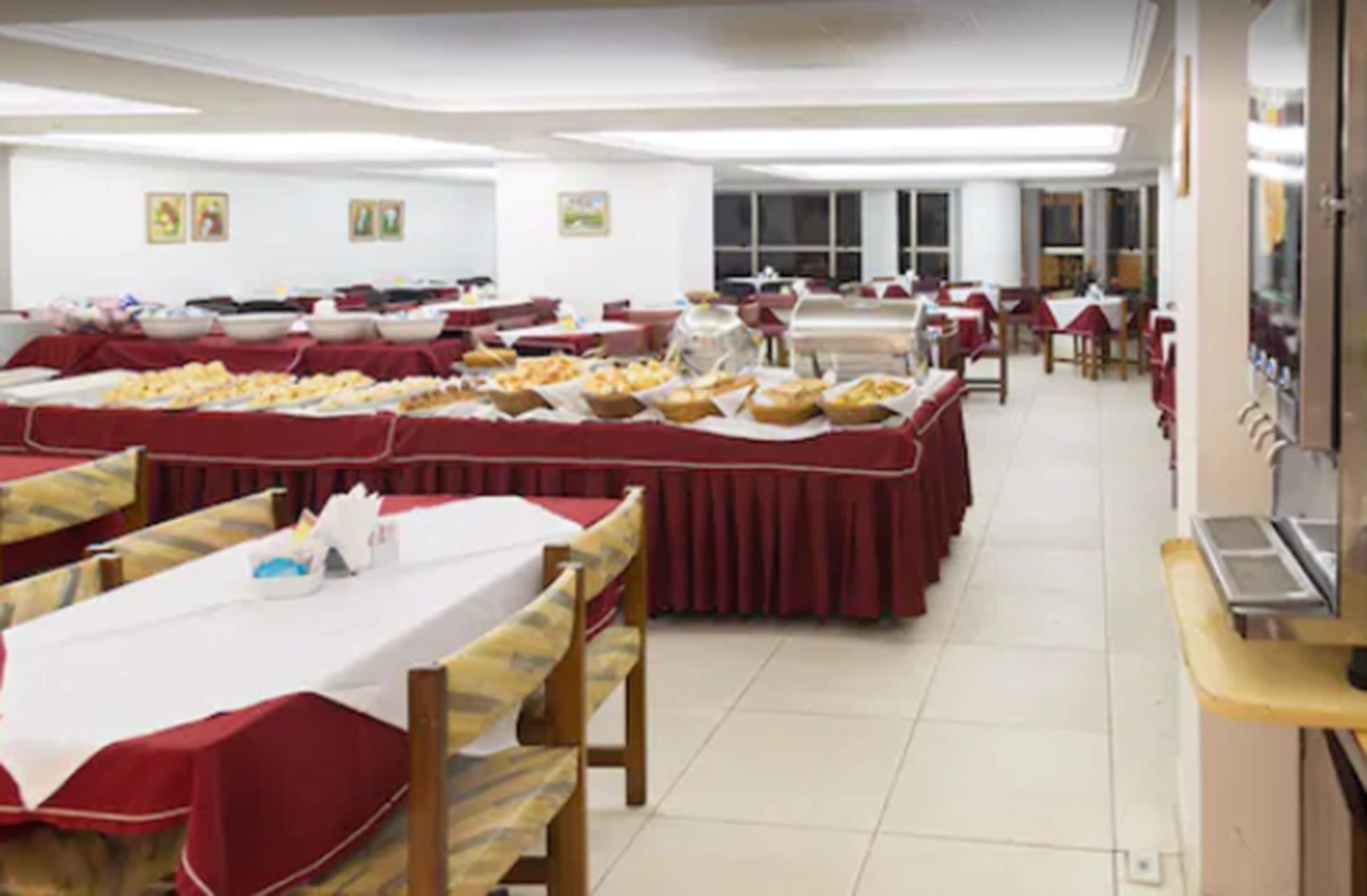 A banquet hall with multiple tables covered in red tablecloths, each with a variety of food items.