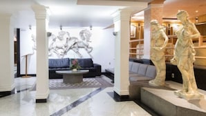Un hall d’entrée orné de colonnes en marbre, avec un canapé, une table basse et deux statues en marbre.