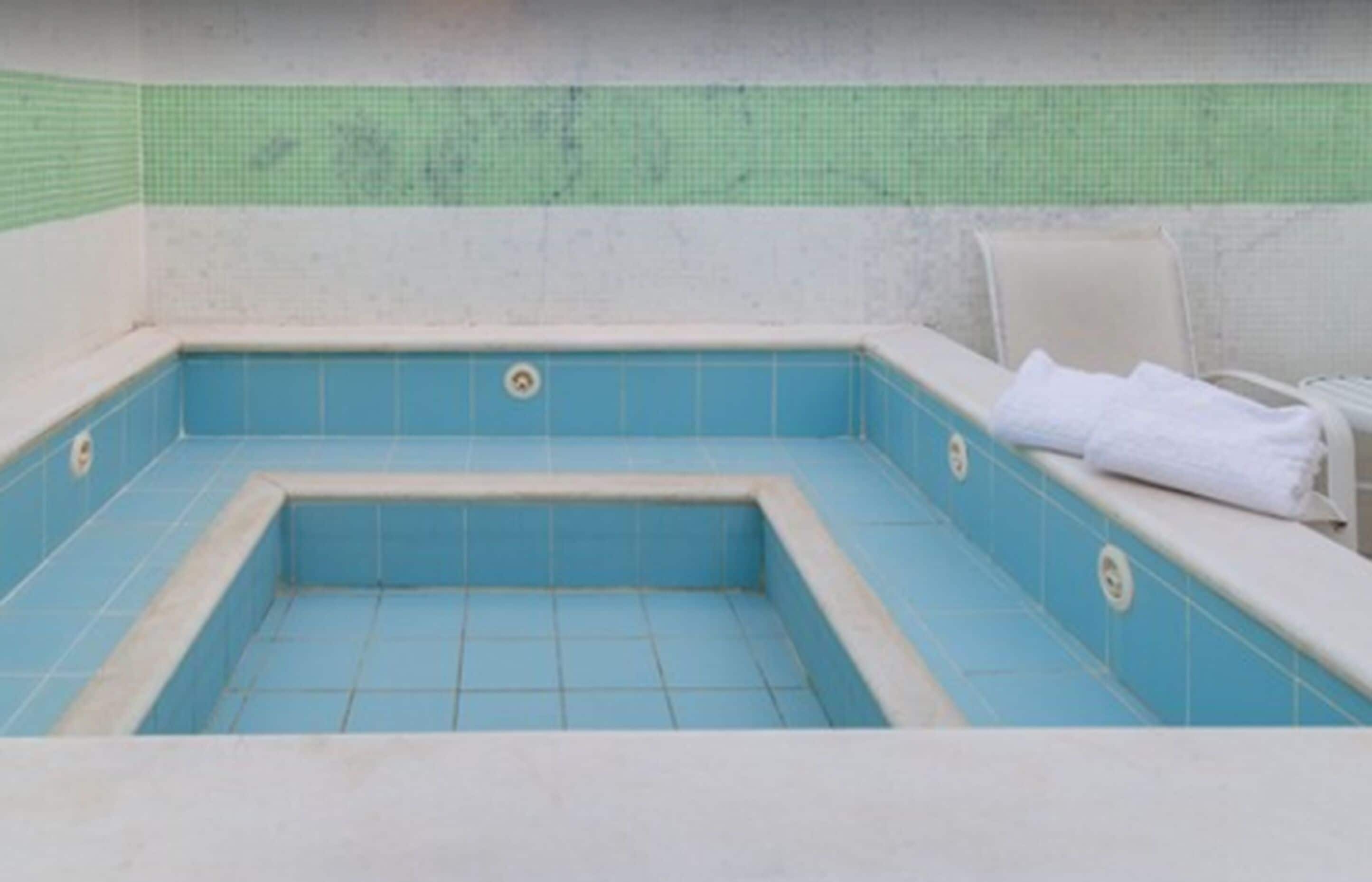 A small, enclosed pool area with a tiled floor and walls, a bench with a towel, and a green-tiled wall behind the pool.