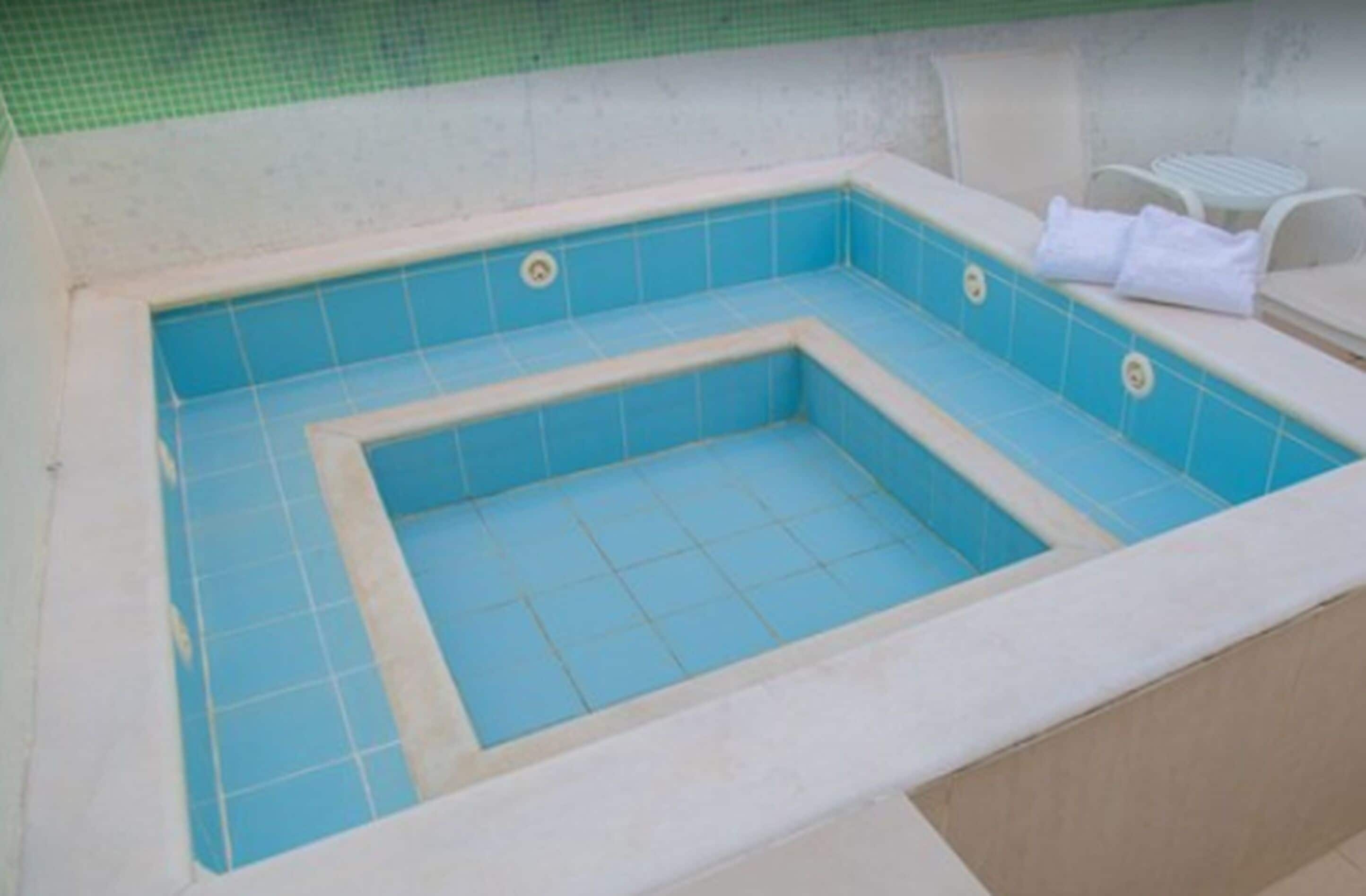 Tinaja rectangular con azulejos azules y un borde blanco, rodeada por una pared color beige y una zona con baldosas verdes.