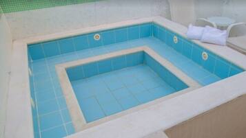 Tinaja rectangular con azulejos azules y un borde blanco, rodeada por una pared color beige y una zona con baldosas verdes.