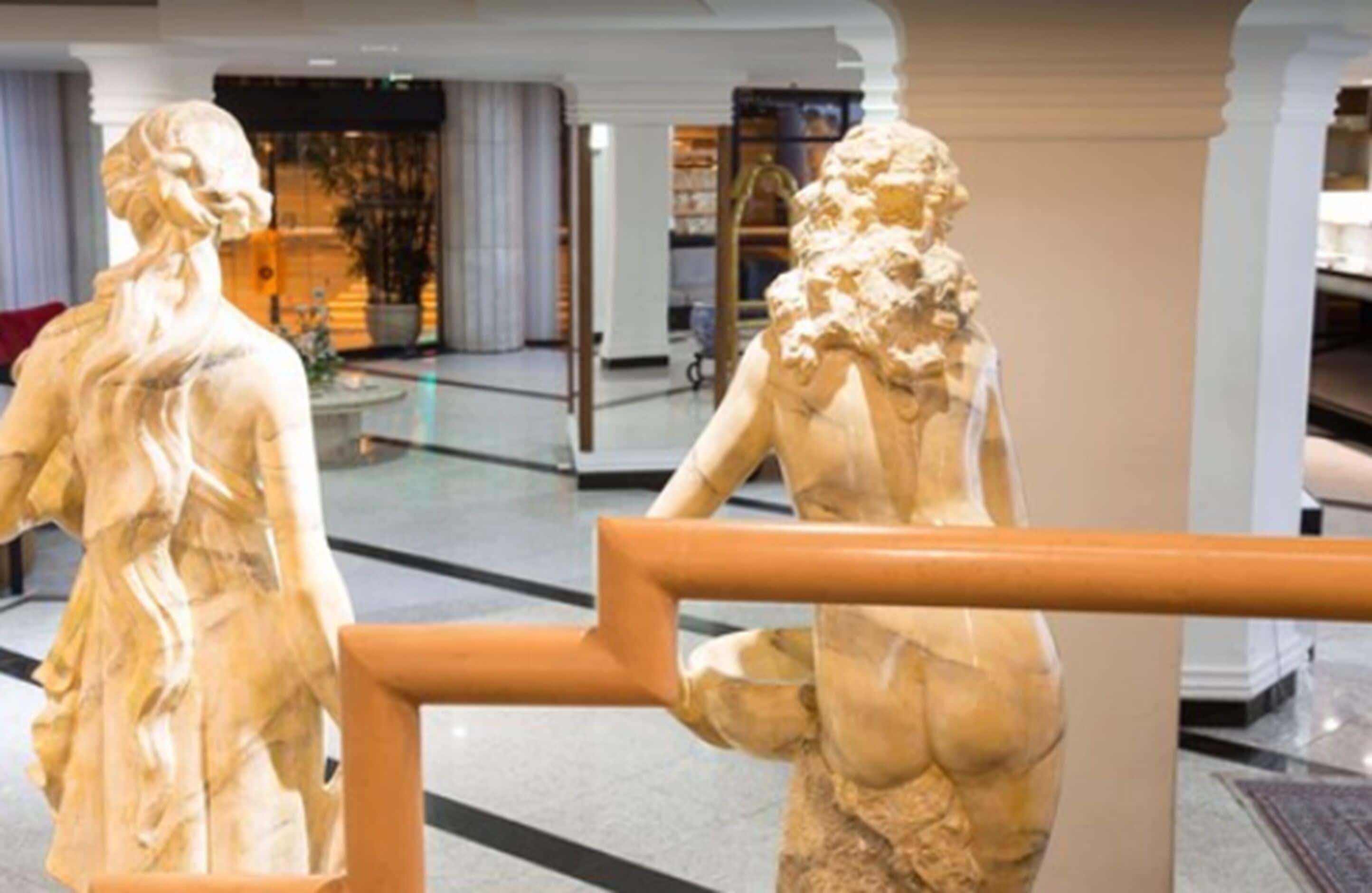 Marmorstatuen in einem Eingangsbereich mit Glastrennwand und Holzgeländer.