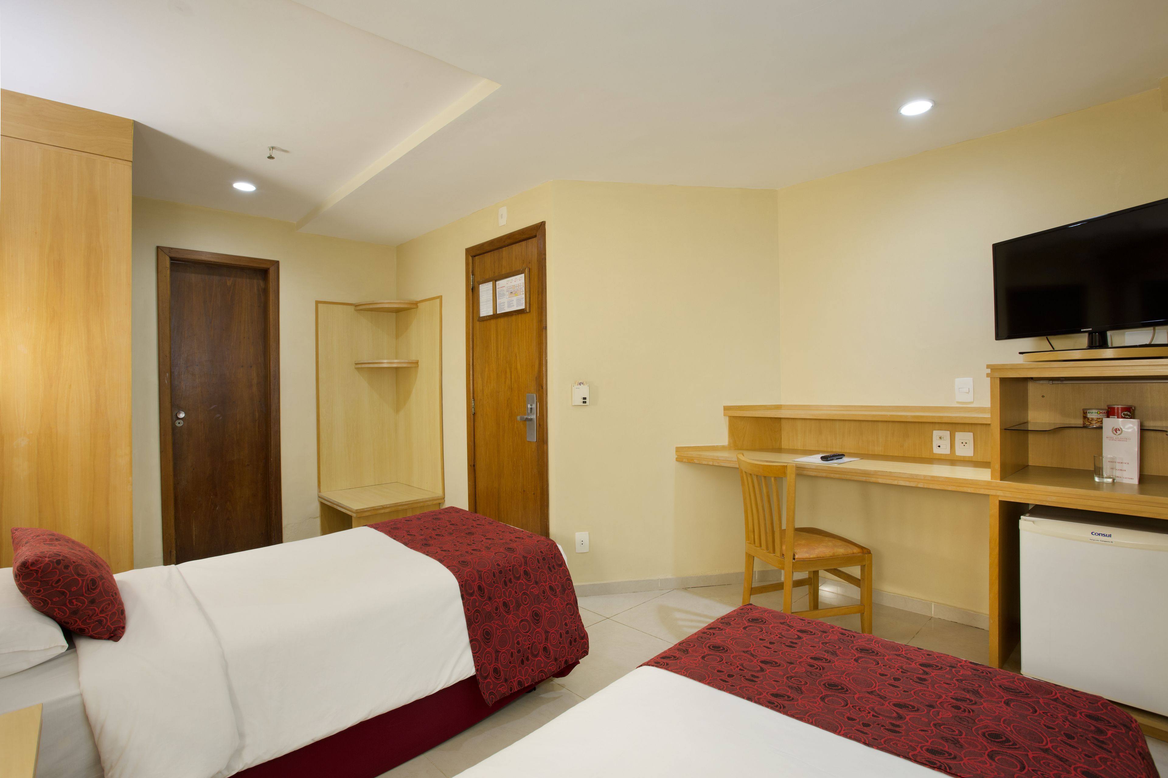 A hotel room with two beds, a desk, a chair, a television, and a refrigerator.