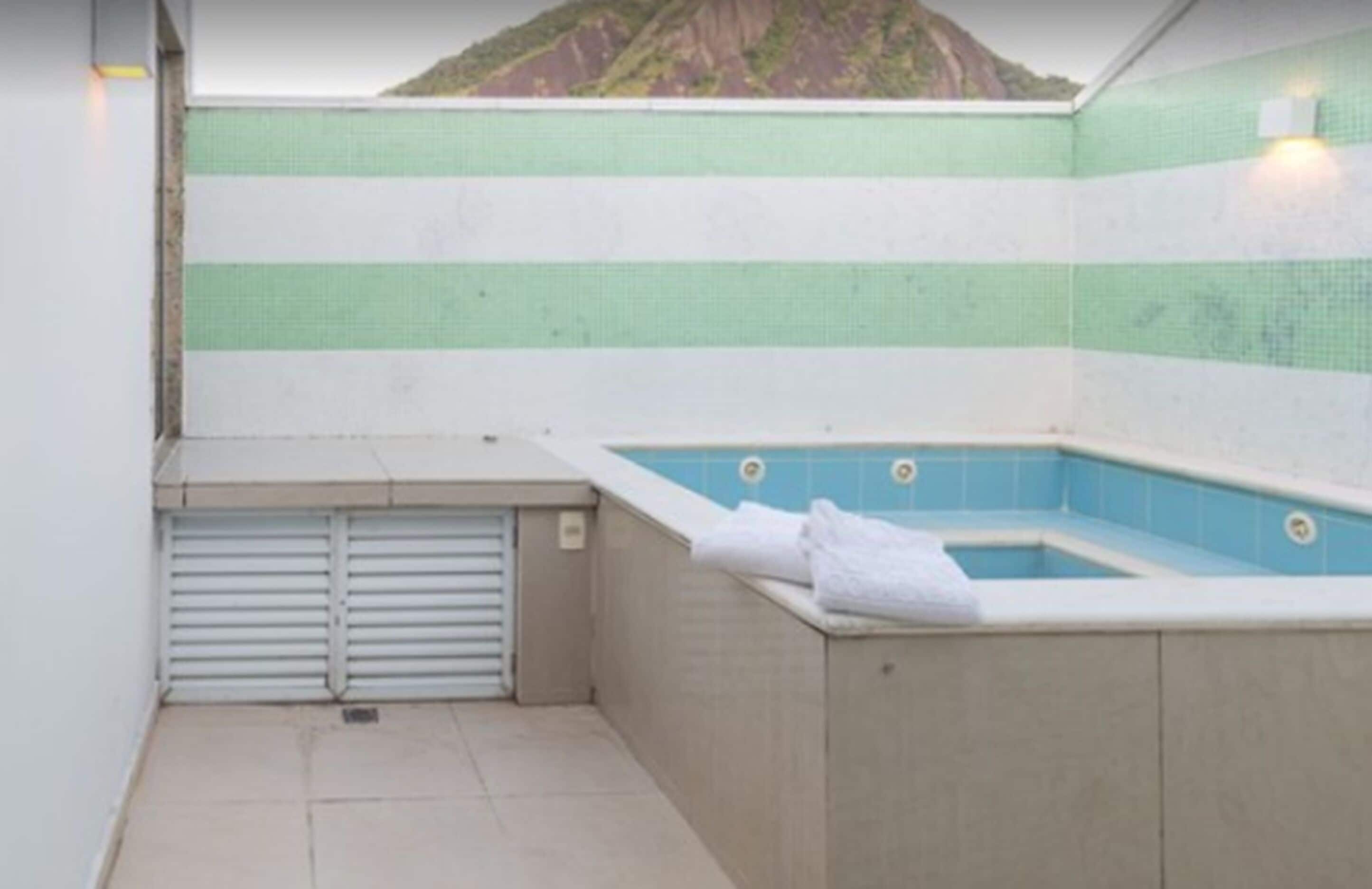 A small, enclosed swimming pool area with a tiled wall and a view of a mountain.