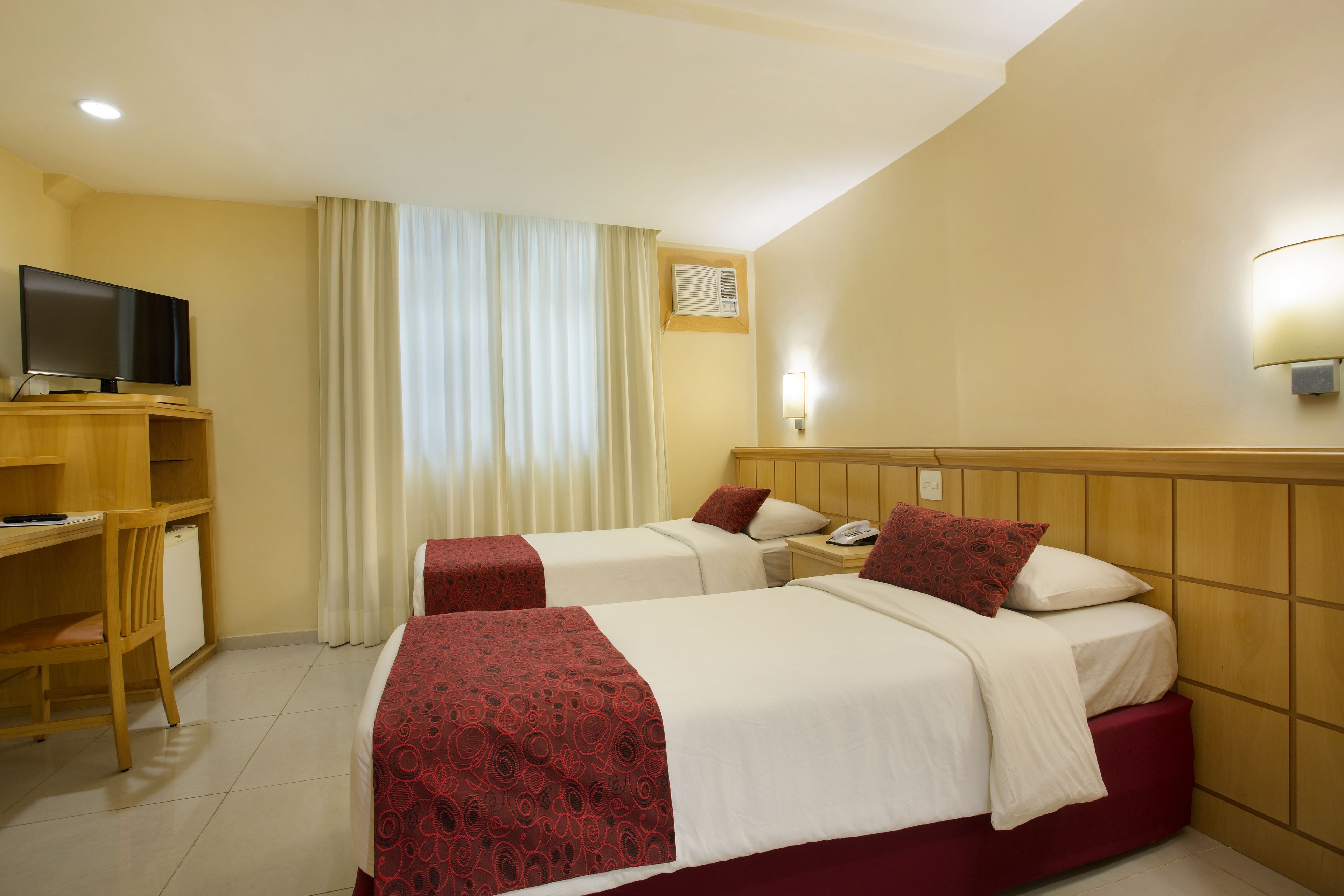 Habitación de hotel con dos camas, un escritorio, un televisor y una ventana con cortinas.