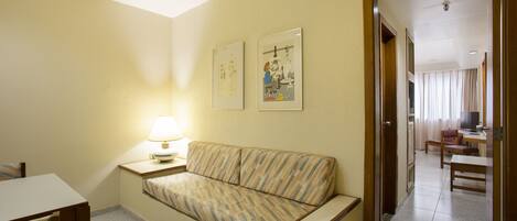 Habitación de hotel con un sofá, una mesa, una lámpara y dos cuadros en la pared.
