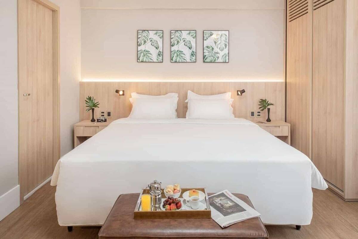 Een hotelkamer met een groot bed, nachtkastjes met lampen, een dienblad met ontbijtartikelen en drie ingelijste foto's aan de muur.