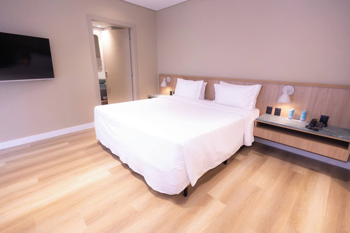 Een moderne hotelkamer met een groot bed, een nachtkastje met een lamp, een aan de muur bevestigde televisie en een houten vloer.