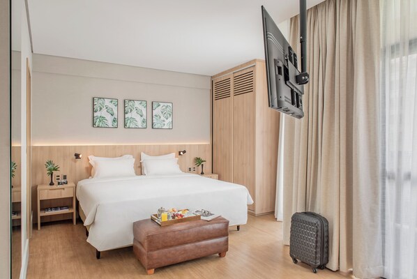 Une chambre d’hôtel dotée d’un grand lit, d’un téléviseur à écran plat fixé au mur, d’une armoire en bois et d’une petite table de chevet avec une lampe.