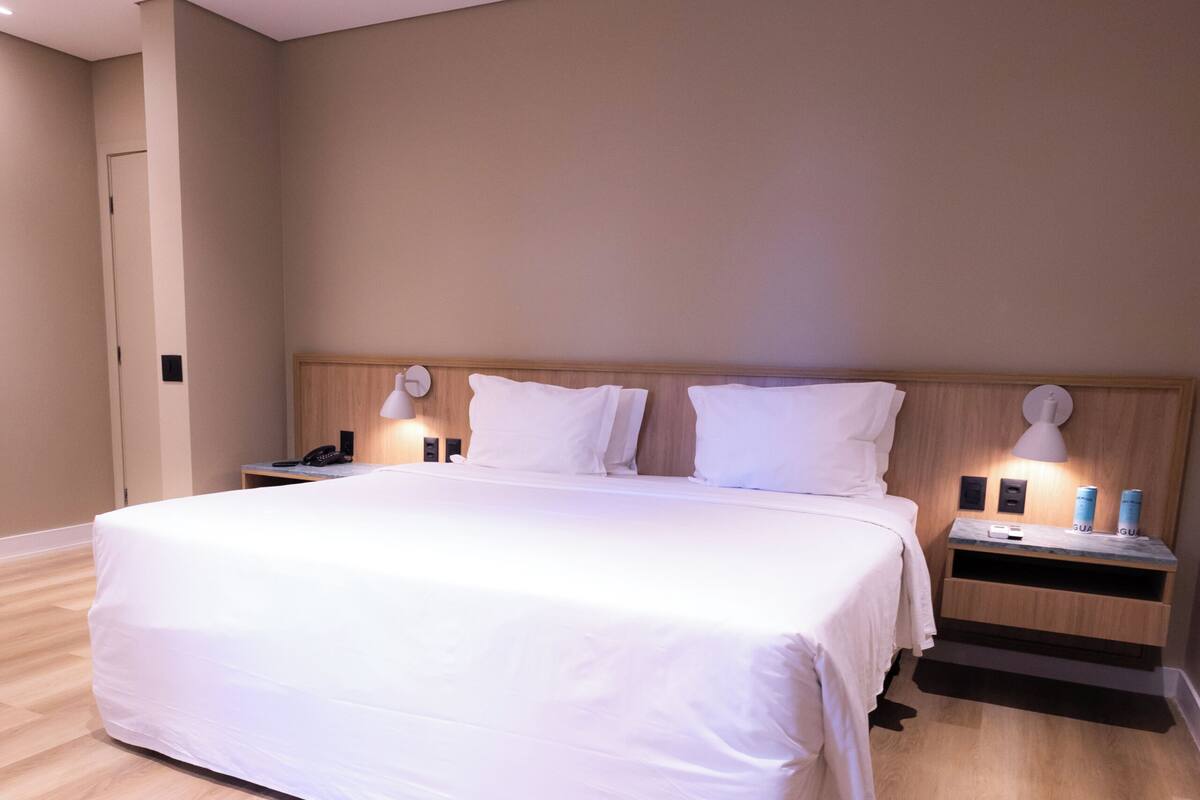 Une chambre d’hôtel moderne avec un grand lit, une tête de lit en bois, des lampes de chevet et une table de chevet.
