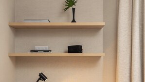 A hotel room with a wooden desk, a chair, a desk lamp, a small plant, and a wall-mounted air conditioner.