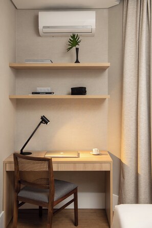 Ein Hotelzimmer mit einem Holztisch, einem Stuhl, einer Schreibtischlampe, einer kleinen Pflanze und einer Wand-Klimaanlage.