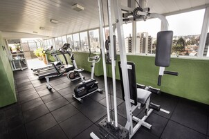 Un gimnasio con diverso equipamiento de ejercicio, una pared verde y vistas a edificios a través de amplios ventanales.