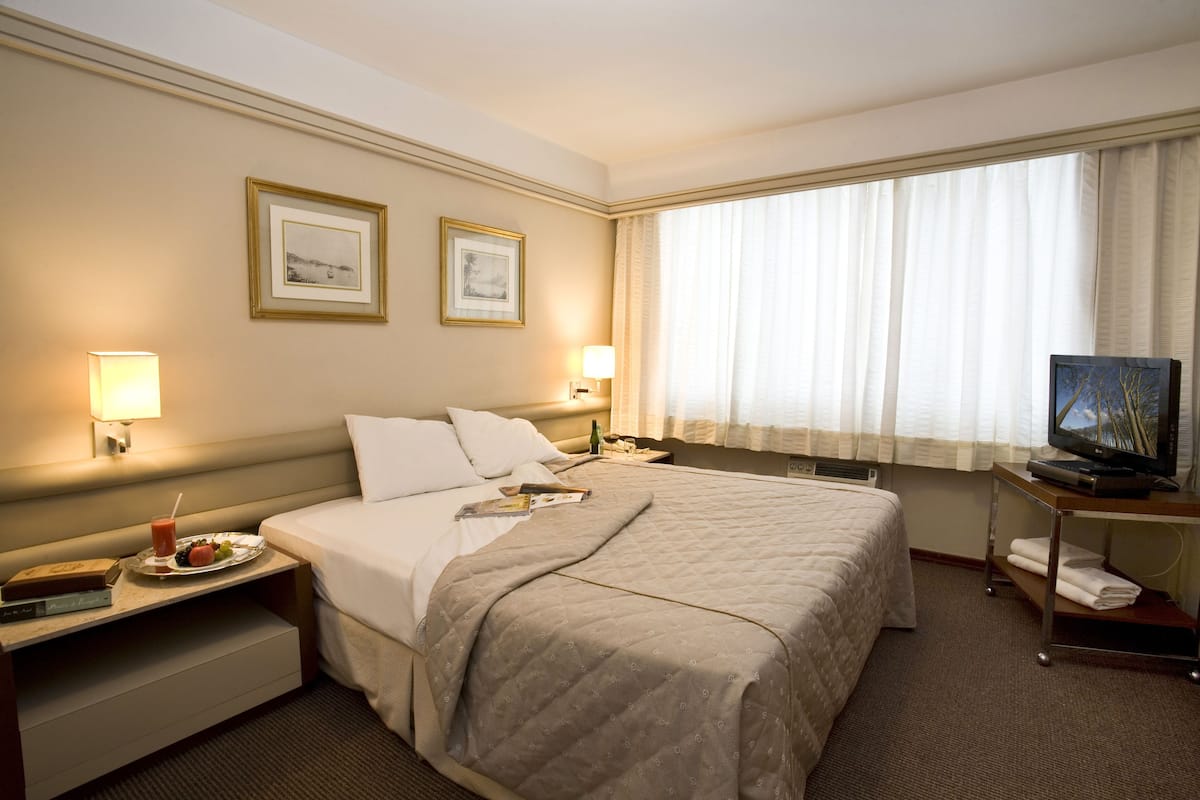 Een hotelkamer met een groot bed, twee bedlampen, een flatscreen televisie, een nachtkastje met een ontbijtplateau en een raam met dunne gordijnen.