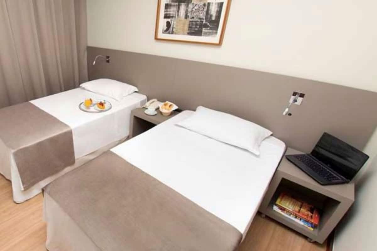 Een hotelkamer met twee bedden, een bureau met een laptop, een nachtkastje met een telefoon en een klein boekenrek.