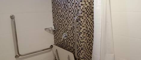 Un baño con paredes de azulejos blancos, una pared de ducha con mosaicos y una barra de apoyo.