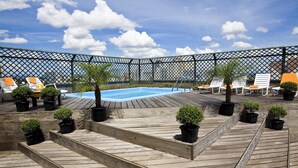 Un área de piscina en la azotea con cubierta de madera, sillas de descanso y plantas en macetas.
