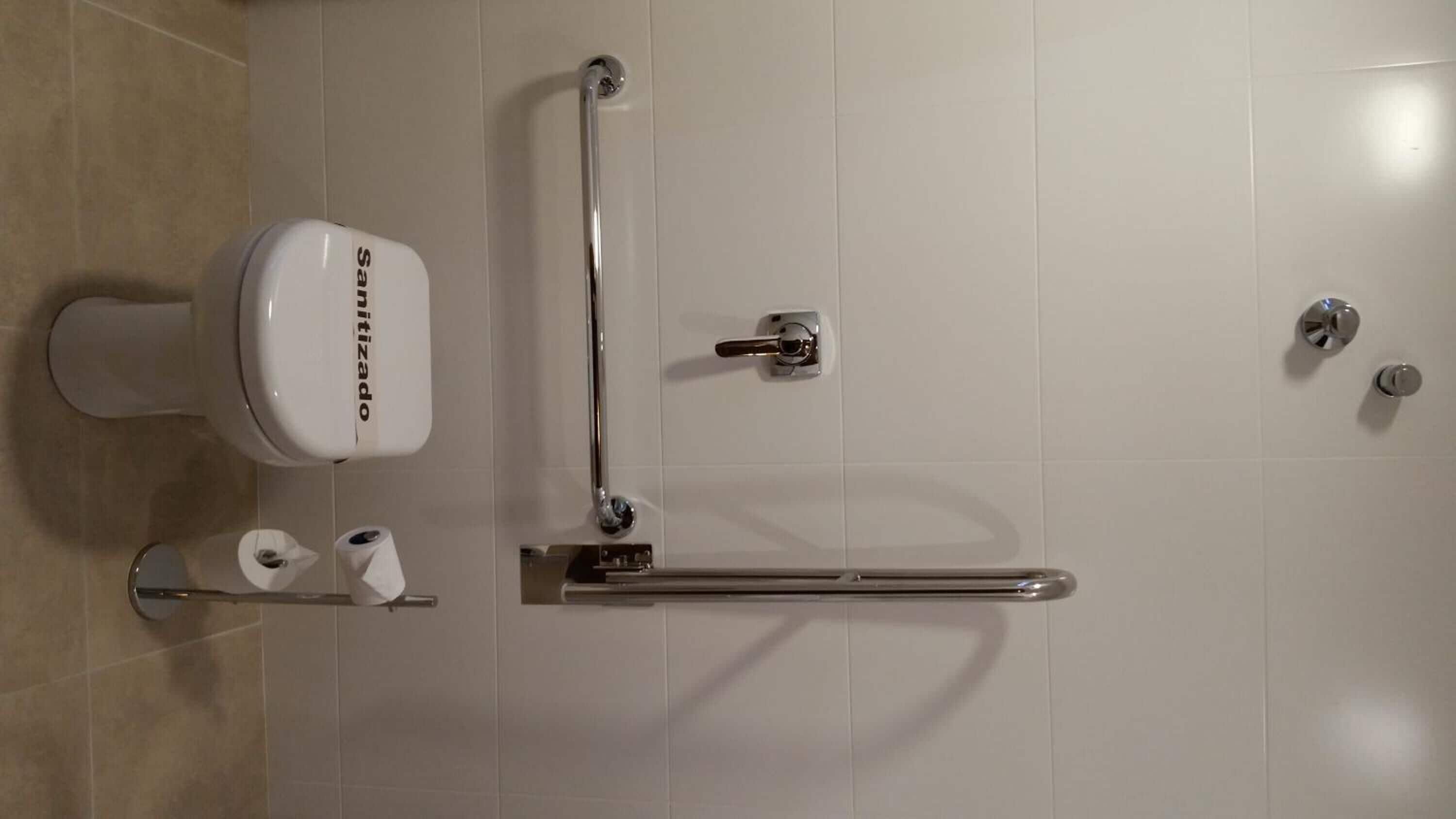 A modern bathroom with a toilet, grab bar, and toilet paper.