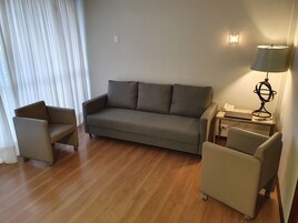 Una sala de estar moderna con un sofá, dos sillones, una mesita con una lámpara y una computadora portátil.