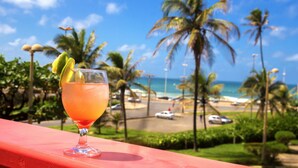A cocktail glass with a lime garnish on a red railing overlooking a beach with palm trees and the ocean. - Bahiamar Hotel (Salvador)
