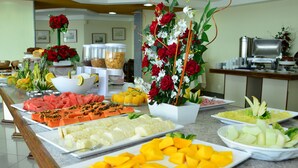 A buffet with various fruits, vegetables, and a decorative floral arrangement. - Bahiamar Hotel (Salvador)