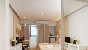 A hotel room with a bed, a desk, a TV, and a window with curtains.