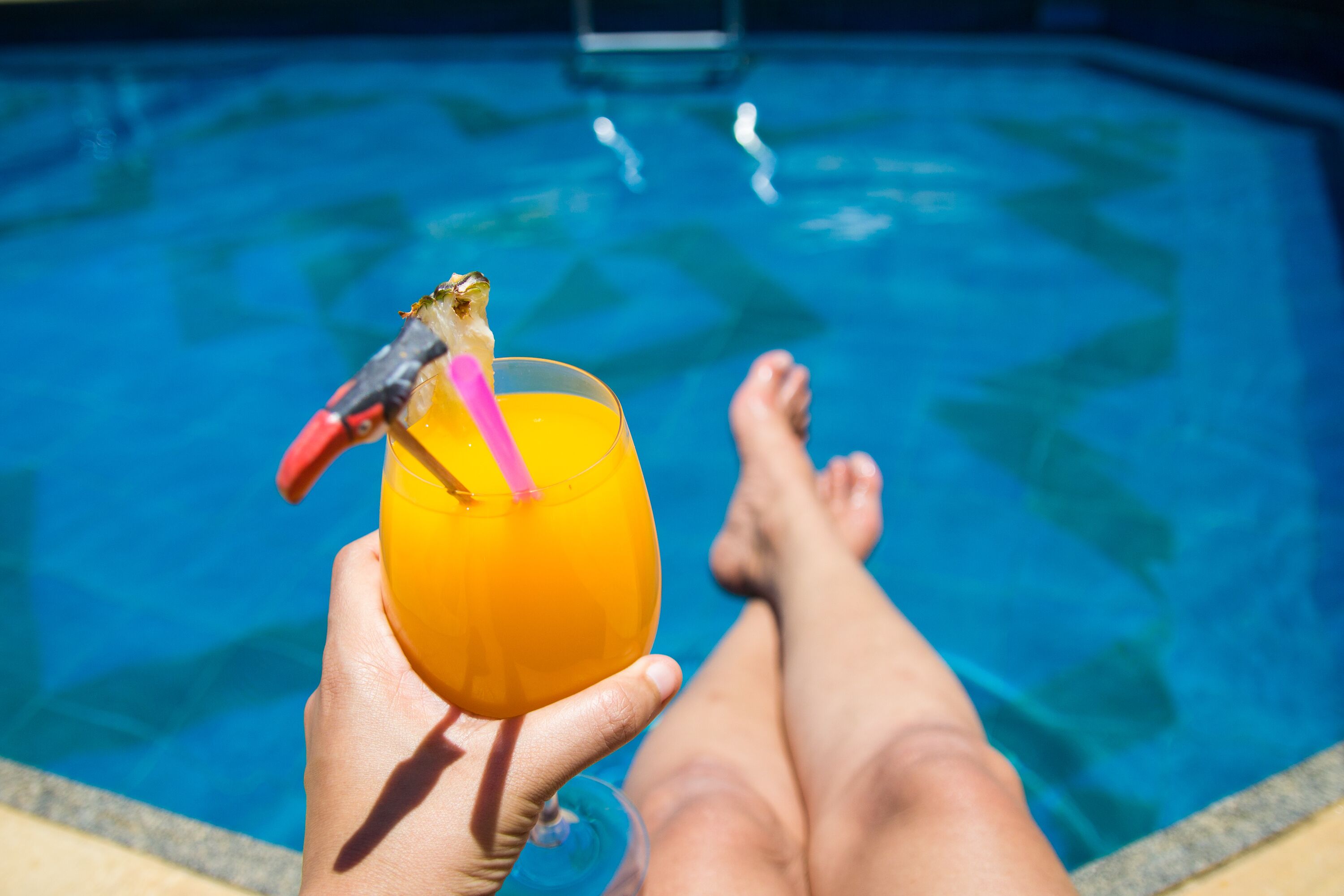 A person relaxing by a pool with a drink in hand.