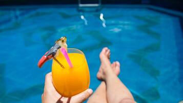 A person relaxing by a pool with a drink in hand.