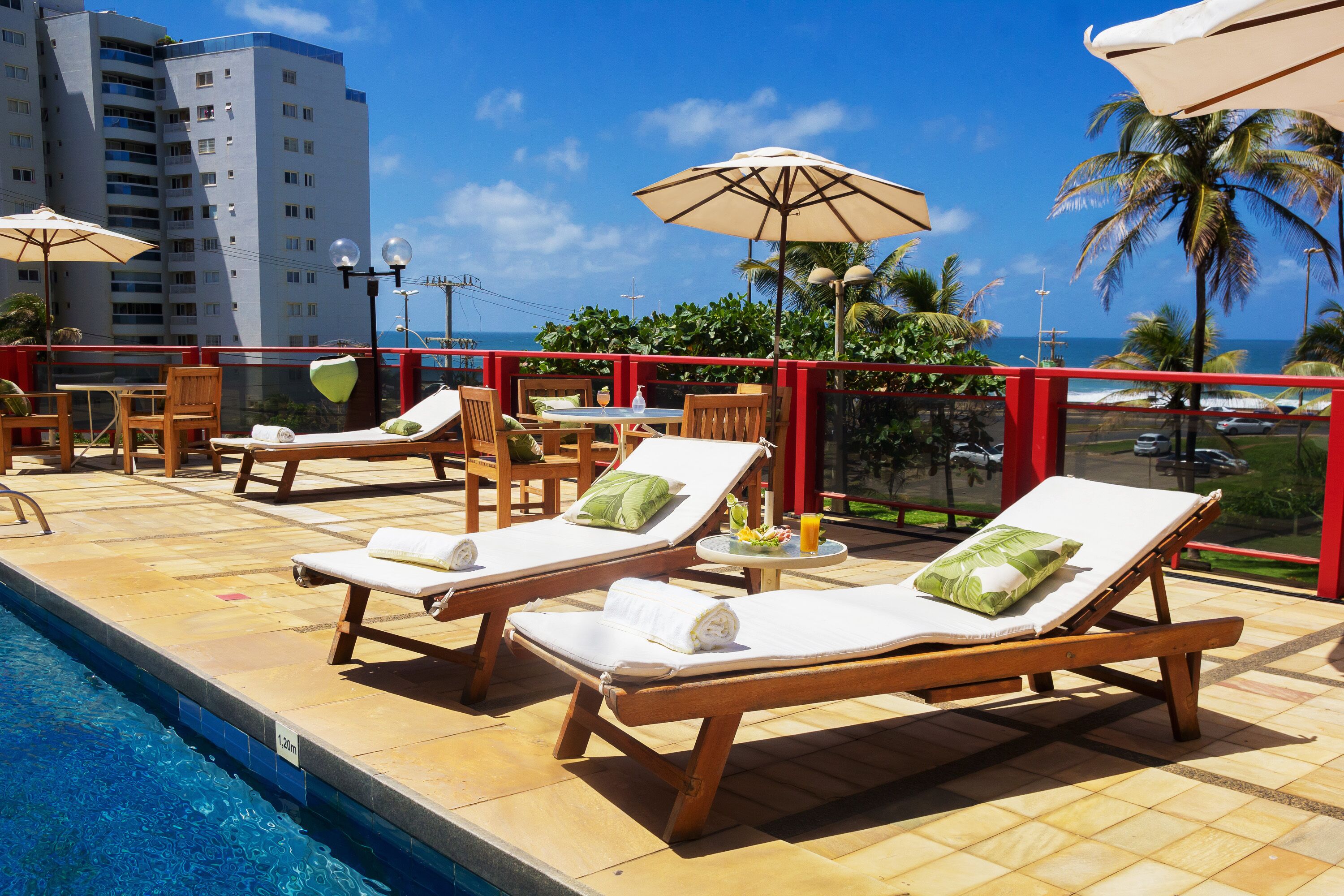 A poolside area with lounge chairs and umbrellas, a clear view of the ocean, and a high-rise building in the background.