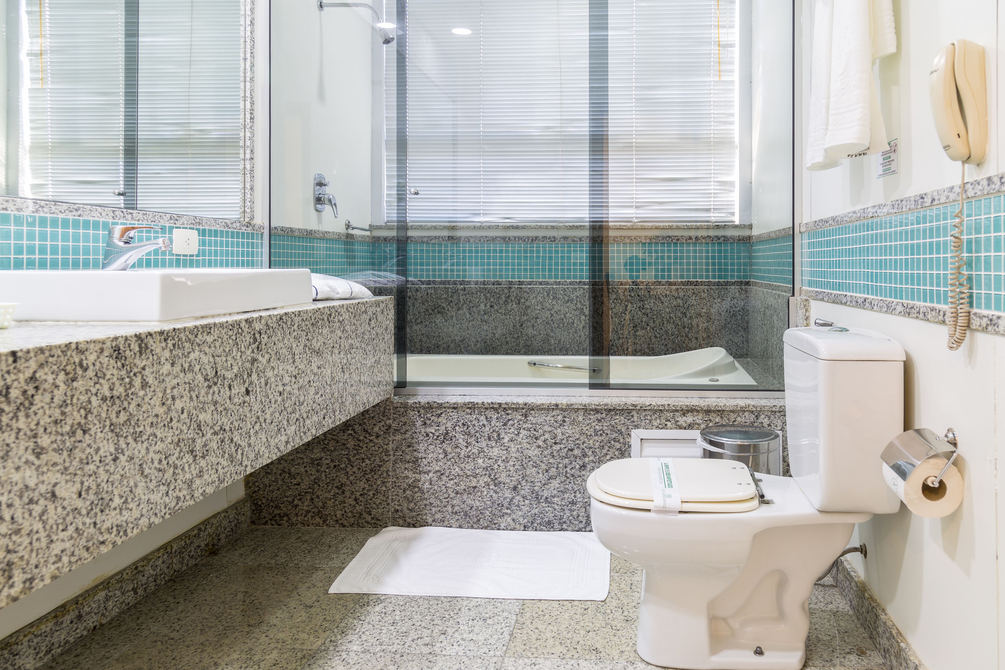 Un baño con encimera de granito, inodoro blanco, bañera y cabina de ducha con paredes de vidrio.