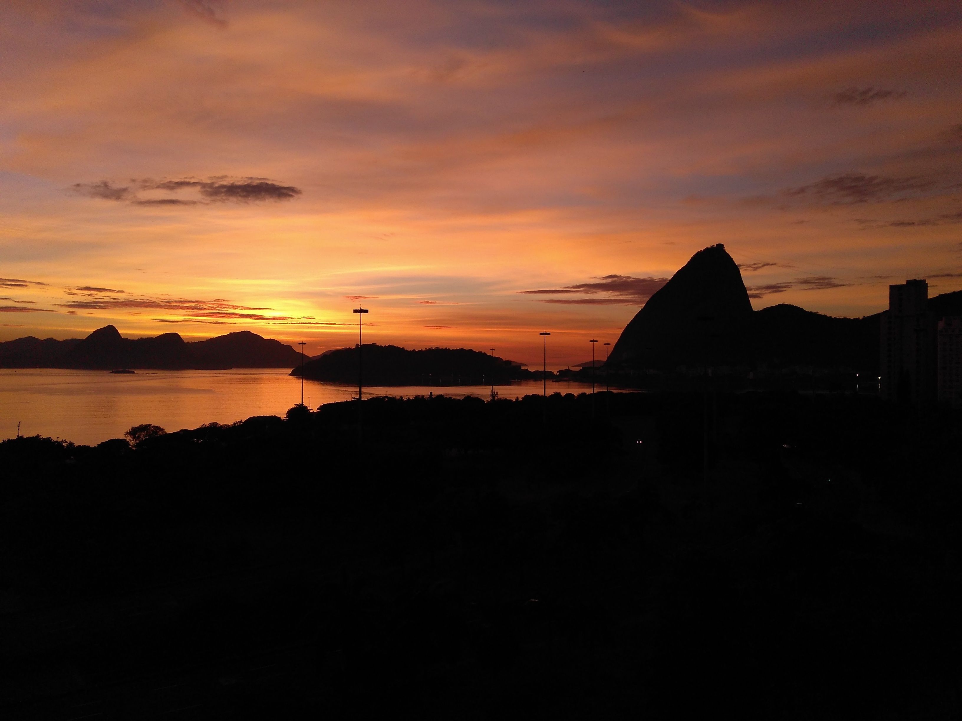A sunset over a body of water with silhouettes of mountains and a prominent building.