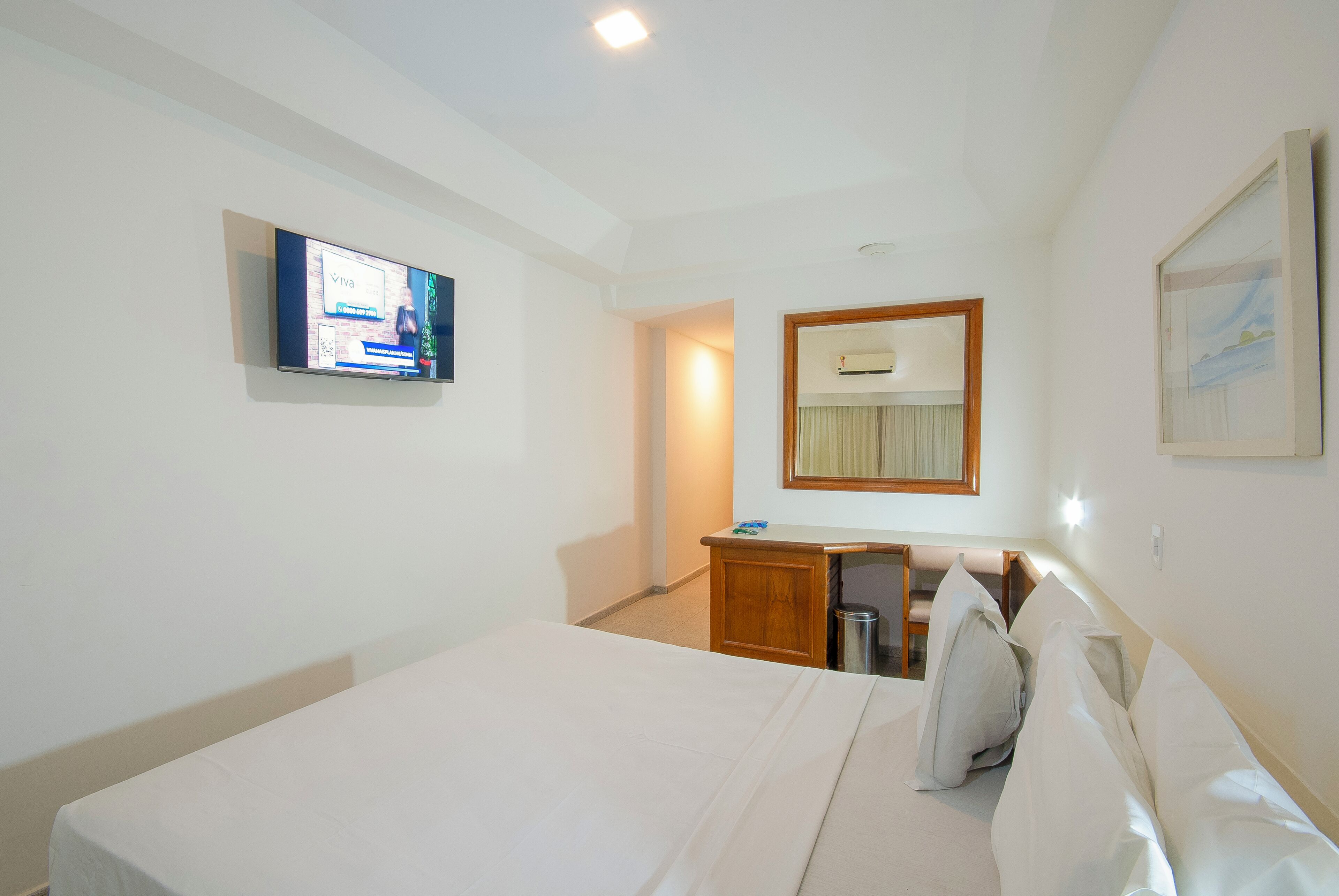 Une chambre d’hôtel avec un lit, un bureau, une télévision, un miroir et un tableau encadré au mur.