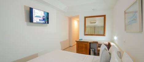 Une chambre d’hôtel avec un lit, un bureau, une télévision, un miroir et un tableau encadré au mur.