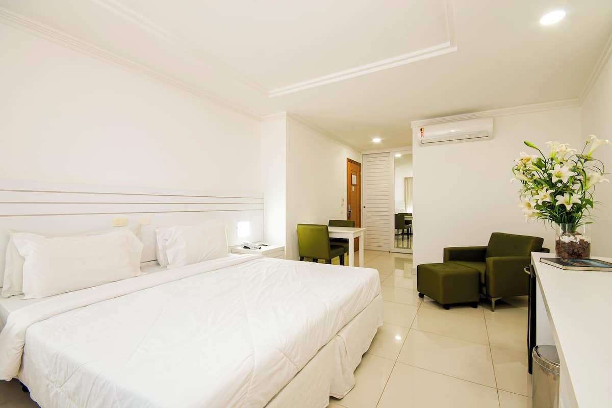 Habitació d'hotel amb un llit gran, un escriptori, dues cadires, una taula petita i un vas amb flors.