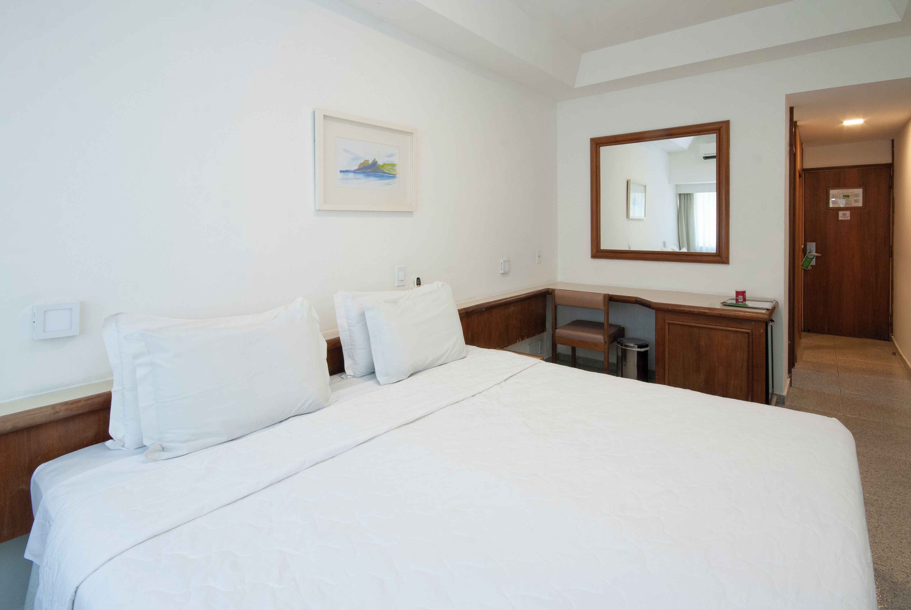 Ein Hotelzimmer mit einem großen Bett, einem Schreibtisch, einem Spiegel und einem Bild an der Wand.