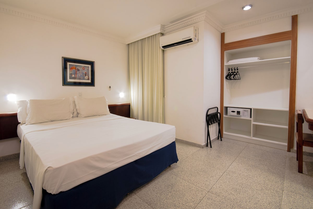 Habitació d'hotel amb llit, una cadira, un armari, aire condicionat i un quadre al mur.