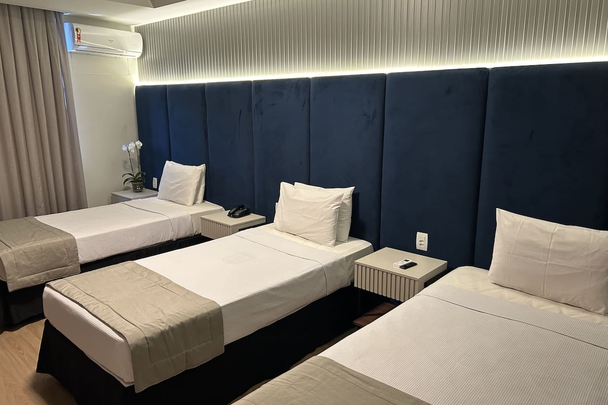 Een hotelkamer met drie eenpersoonsbedden, een nachtkastje met een telefoon en een wandairconditioner.