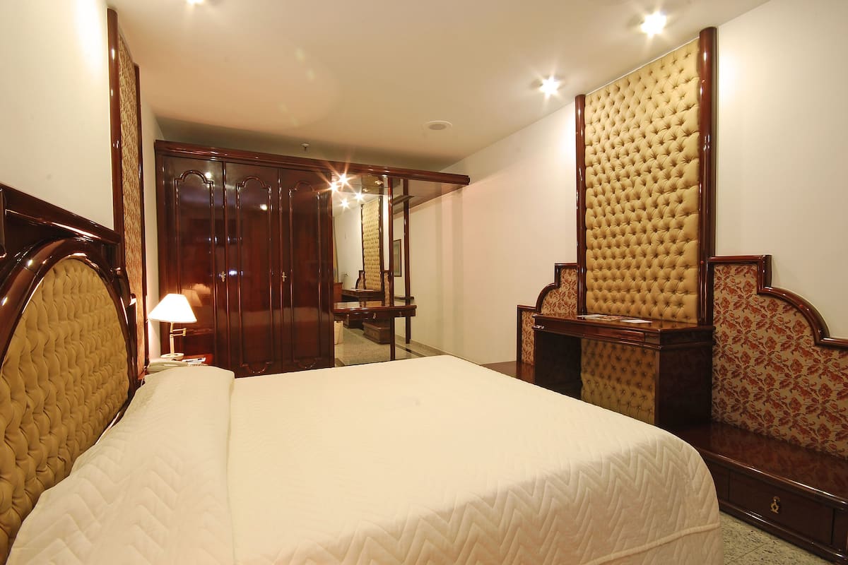 Een hotelkamer met een groot bed, een houten garderobe, een spiegel en een nachtkastje met een lamp.