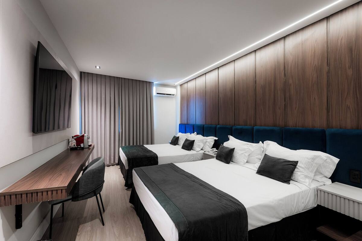 Una habitación de hotel con dos camas, un escritorio, una silla y un espejo grande.